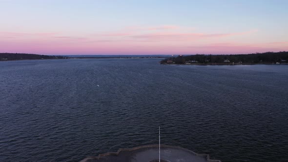 an aerial shot over a bay focused on an island during a beautiful sunrise. It is golden hour and the alt