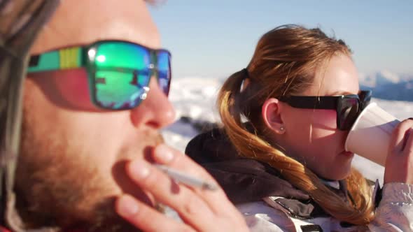 Close Up Footage in Slowmotion of Caucasian Male and Female in Sun Glasses Sitting on Ski Mountain alt