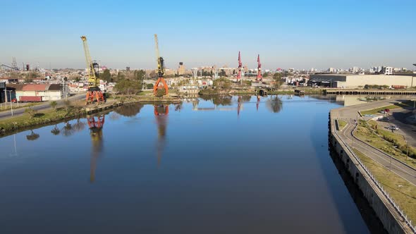 Aerial pull out shot overlooking at industrial cranes at waterfront cargo terminal along Riachuelo M alt