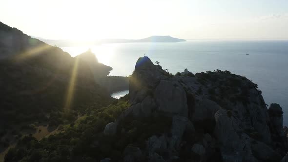 Aerial Silhouette of Young Woman Raising Her Hands Standing on the Top of a Mountain Over the Sea at alt