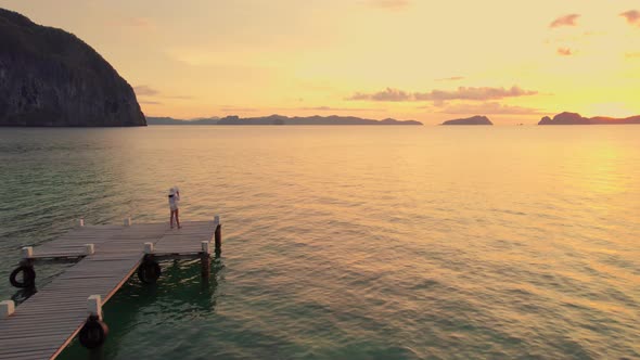 Woman On Wooden Pier As The Sun Sets Over The Ocean alt
