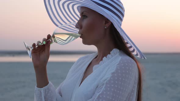 Elegant Woman with Glass of Wine Resting on Beach at Sunset