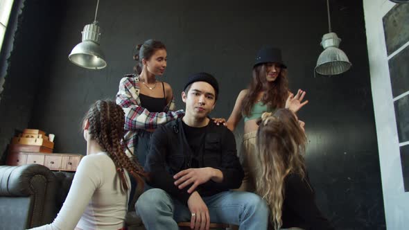 The Guy is Sitting on a Chair While the Young Pretty Girls are Dancing Around Him alt