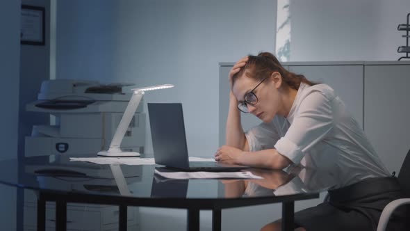 Young Tired Businesswoman Looking Unhappily at Laptop Display Analyzing Financial Data in Office alt