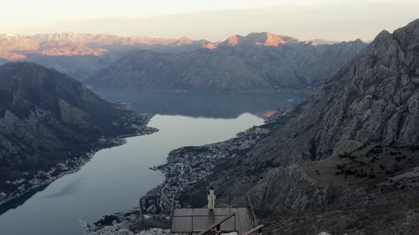 Woman in traditional Montenegrin dress standing on wooden deck and enjoying the birds eye view of Ko alt