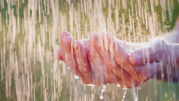 A Man Holds His Hands in the Pouring Rain, Drops of Water Fly Apart alt