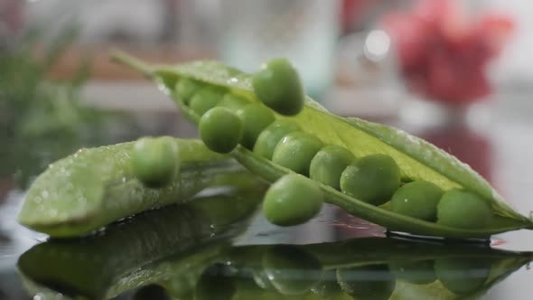 Green Peas Falling Into Table Beside Its Open Pod. - close up, slow motion alt