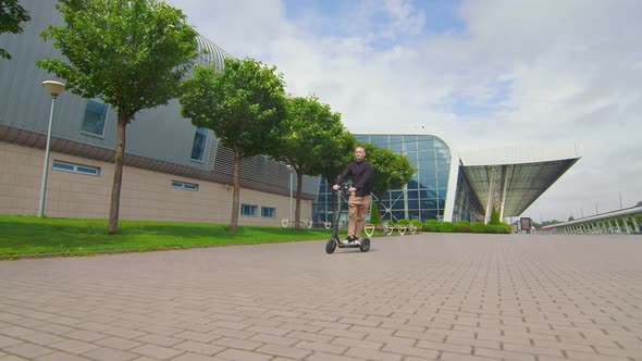 Successful Young Man Rides an Electric Scooter Near the Business Center. Young People on an Electric alt