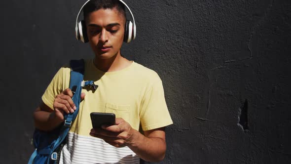 Mixed race man wearing headphones and using smartphone in the street alt