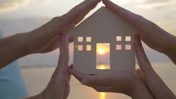 Hands Holding House Silhouette Against Sun alt