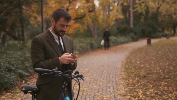 Handsome young man with electric bicycle using mobile phone in the autumn park