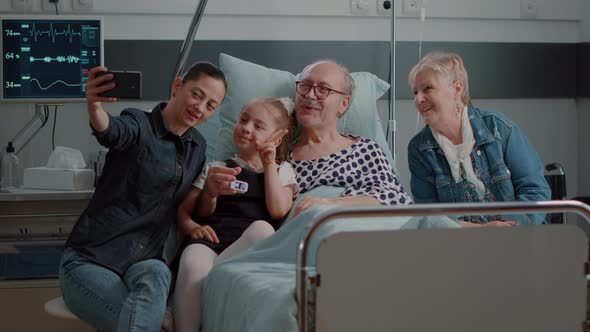 Family Visiting Retired Man and Taking Selfies in Hospital Ward alt