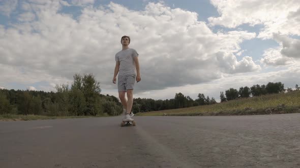 young man is riding longboard on country road on backgroundof beautiful sky with clouds alt