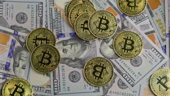 Rotating Bitcoin Coins Scattered Over US Dollar Banknotes Closeup