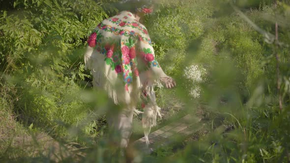 Beautiful Overweight Woman with a Wreath on Her Head and Flowers in Hands Going Through the Small alt