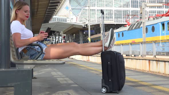 A Young Beautiful Woman Works on a Smartphone on a Train Station Platform alt