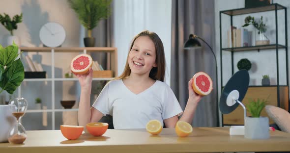 Girl Sitting in front of Camera at Home and Playing with Halfs of Grapefruit alt