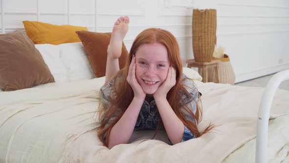 Funny Red-haired Girl with Freckles Smiling on Bed alt