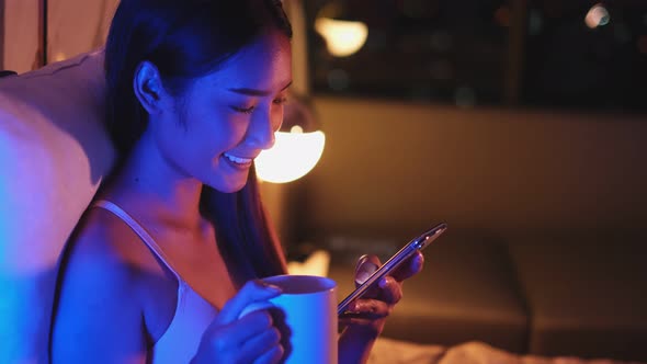 Young Asian beautiful woman enjoy using smartphone in bedroom at night time. alt