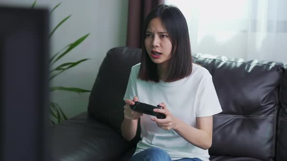 Woman sitting on sofa and holding joystick with playing games in the living room at home alt