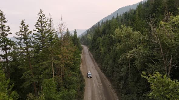 Drone footage of a car driving through a dry boreal forest in British Columbia at sunset. Aerial opp alt