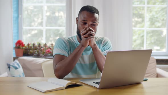 Ethnic Young Man Sitting at Table with Laptop and Working on Remote Project at Home alt