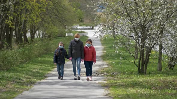 A mother and two daughters walk in a spring Park in medical masks. 