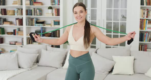 Young Woman is Standing in the Living Room Getting Ready to Do Exercises with an Expander Looking at