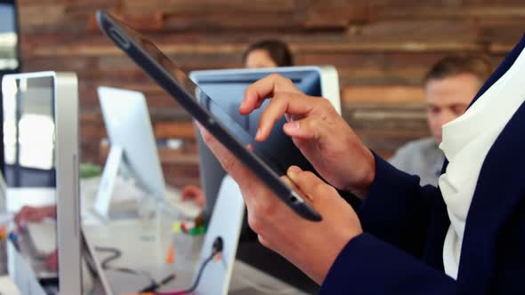 Female business executive using digital tablet while colleague working at desk alt