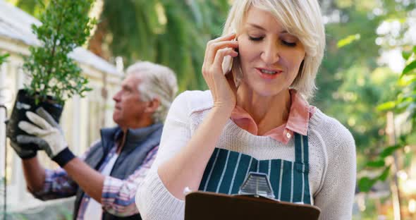 Mature woman talking on phone while man checking vegetables alt