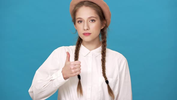 Portrait of Young Cute Woman Isolated Over Blue Background Wall Looking on Camera and Showing Thumb alt