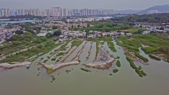 A dynamic aerial footage of the fishing village in Lau Fau Shan in the foreground and the big city o alt