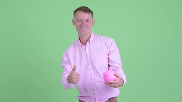 Happy Businessman Holding Piggy Bank and Giving Thumbs Up alt