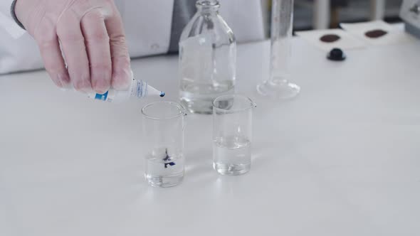 Scientist Add Blue Substance to the Transparent Liquid in Glass Bulb and Mix It on the Lab Desk