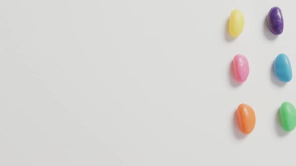 Video of overhead view of rows of multi coloured sweets with copy space over white background alt