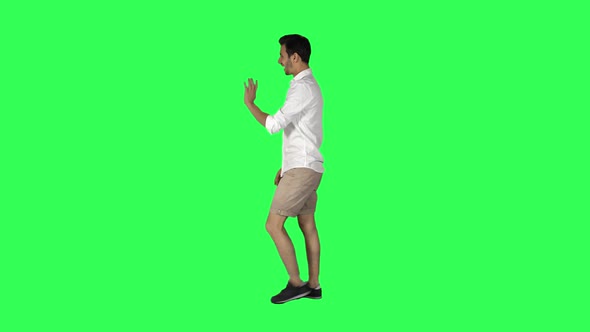 Young man walking and looking around the street, waving hello, over a green screen. 4K alt