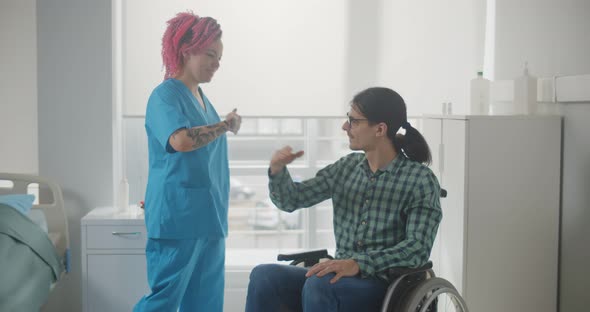 Smiling Female Nurse and Male Patient in Wheelchair Sharing Secret Hand Gesture alt