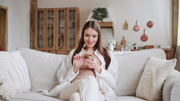 Cheerful Pregnant Woman Texts with Friend Via Smartphone alt