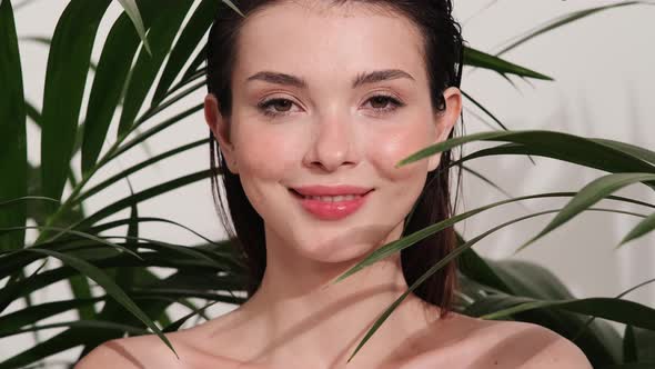 A close-up view of a smiling brunette woman posing with tropical leaves alt