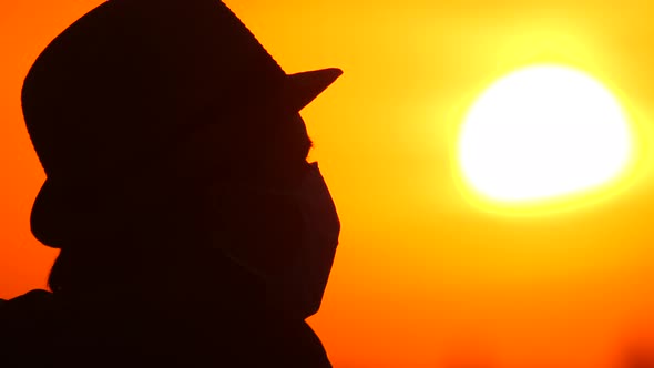 Guy in a Medical Mask on a Background of Sunrise, Sunset. Silhouette of a Turist in a Protective