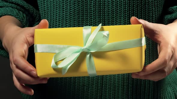 Girl hand holds a gift wrapped in yellow paper tied with white ribbon at a holiday party