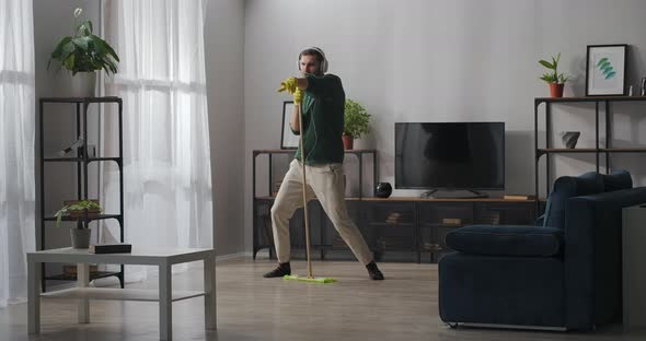 Single Man Is Having Fun During Cleanup at Home Washing Floor and Singing Into Mop Listening To alt