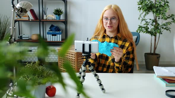 Joyful Girl Recording Video About Modelling Clay Speaking and Waving Hand Looking at Smartphone alt