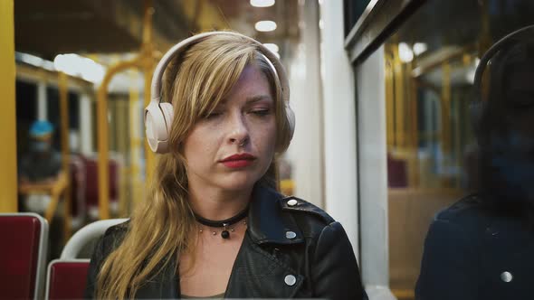 Pensive Bonde Lady Hipster in Headphones is Riding a Tram Sitting on Seat Looking Out the Window and alt