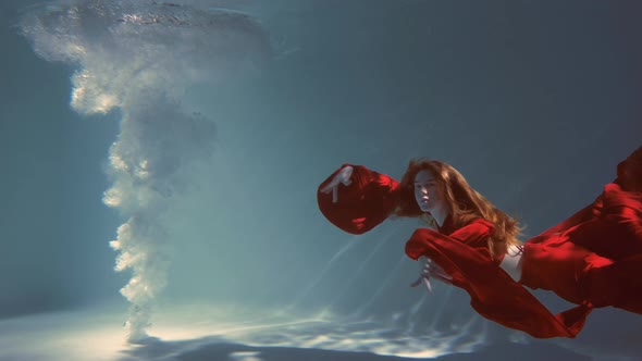 Attractive Redhaired Young Woman Swims Beautifully Underwater in a Red Dress alt
