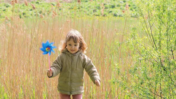 Cute Little Girl Smiles and Looks at Windmill Toy Run in the Field