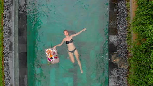 Aerial Shot of a Young Woman Tourist Has Her Own Personal Breakfast on a Floating Table alt