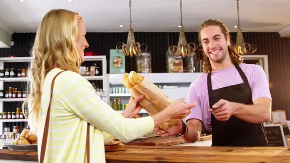 Waiter giving bread roll package to customer at counter alt