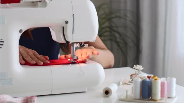 Closeup Seamstress Woman Hands Sewing Red Cloth on Sewing Machine in Workshop alt