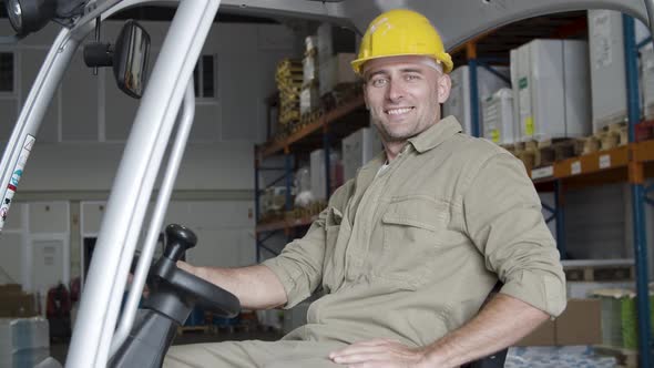 Cheerful Male Factory Worker Sitting in Forklift in Warehouse alt